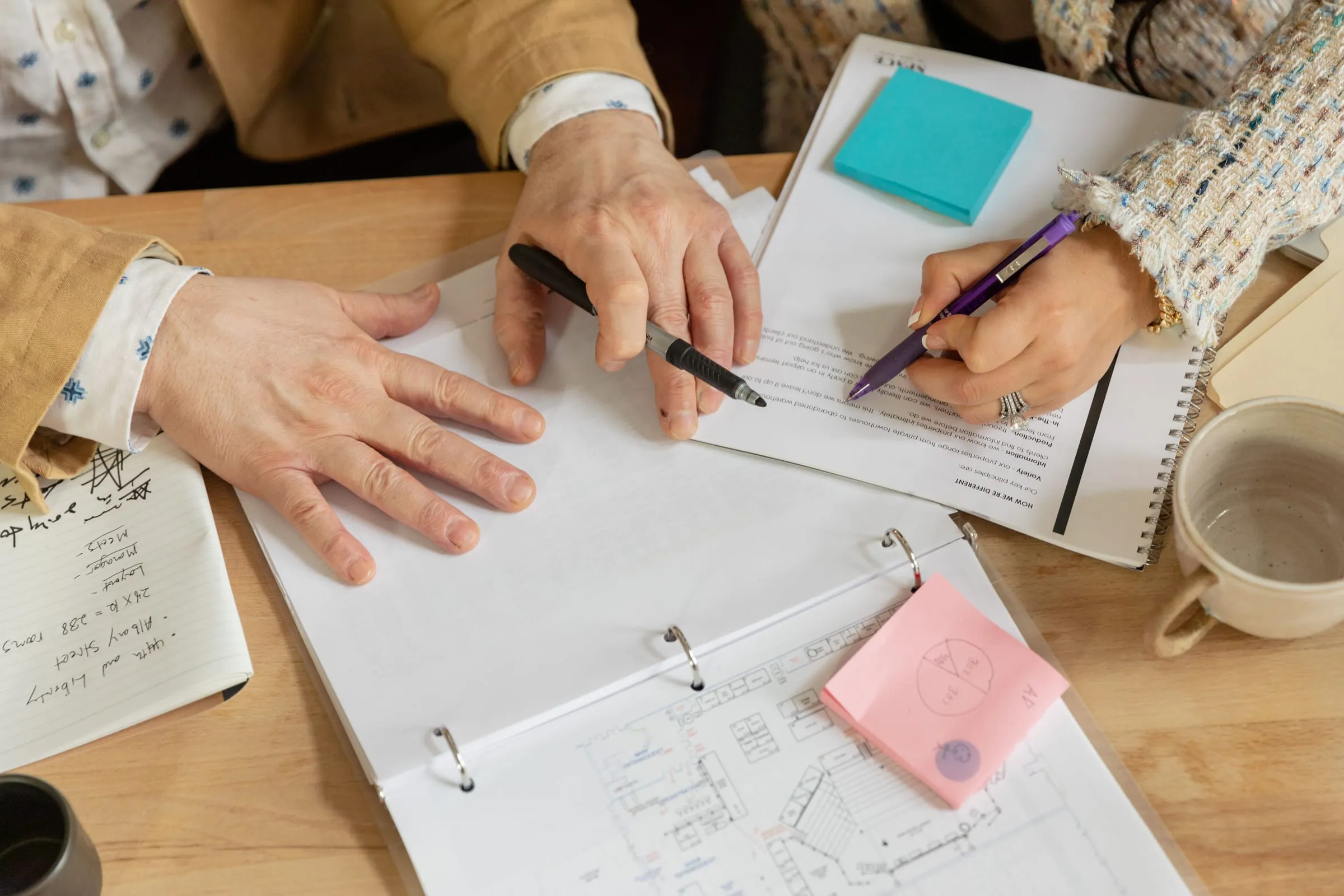 Two people reviewing and annotating printed documents at a desk