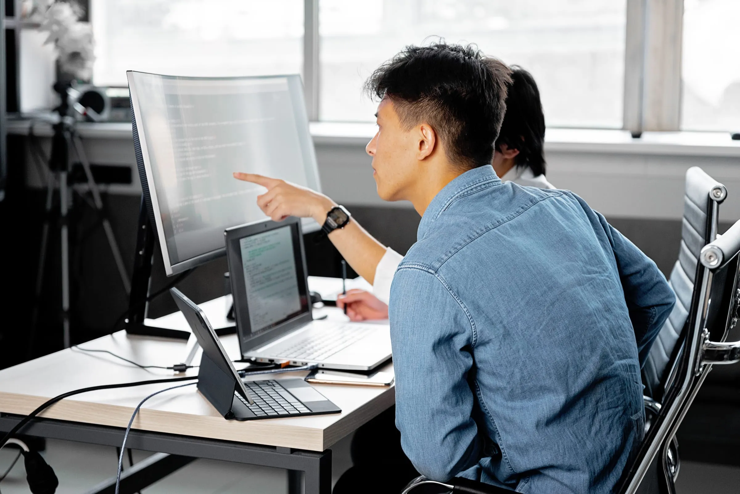 A developer pointing at code on a monitor while working at a desk